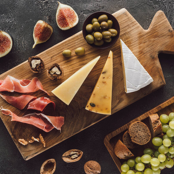 flat lay with assorted cheese, jamon and fruits on dark surface