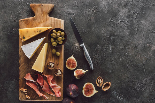 flat lay with assorted cheese, jamon and figs on dark surface