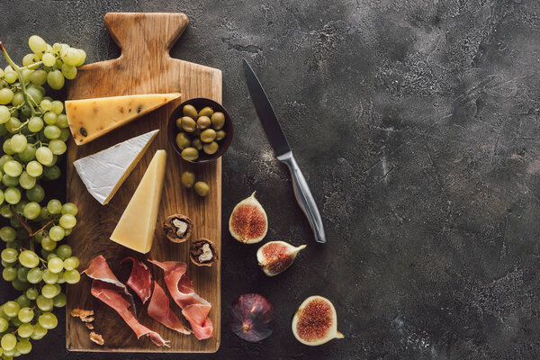 flat lay with assorted cheese, jamon, grape and figs on dark surface