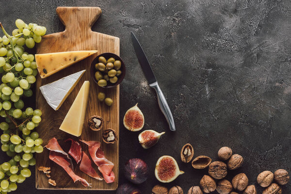 flat lay with assorted cheese, jamon, grape, hazelnuts and figs on dark surface