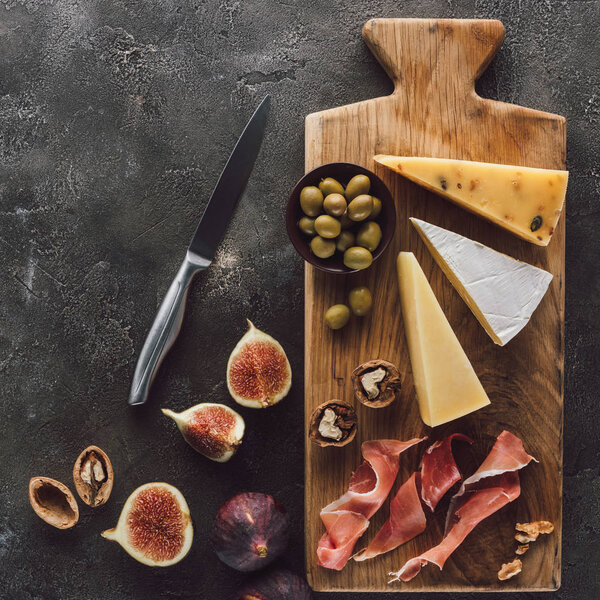 flat lay with assorted cheese, jamon, olives and figson dark surface