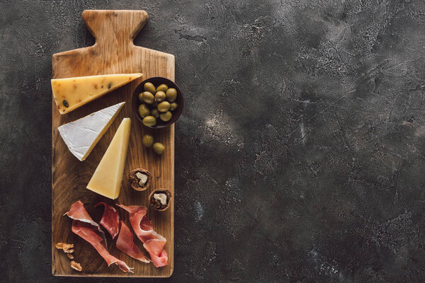 flat lay with assorted cheese, jamon and olives in bowl on dark surface