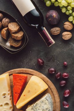 Gıda kompozisyonu şişe şarap, üzüm, ekmek parçaları ve karanlık yüzeyinde çeşitli peynir