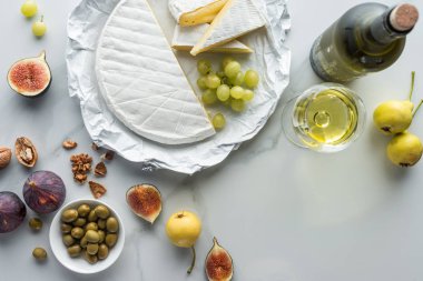 düz lay zeytin, camembert peyniri, şarap ve beyaz mermer yüzey üzerinde düzenlenmiş meyve ile