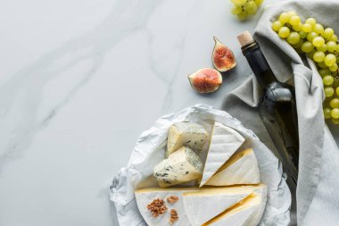 flat lay with assorted cheese, bottle of wine and fig pieces on white marble surface