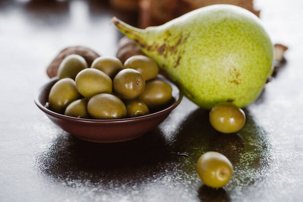 close up view of pear and olives in bowl arranged on tabletop