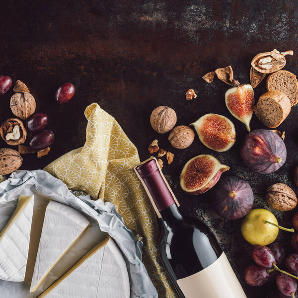 food composition with camembert cheese, bottle of wine and fruits on dark tabletop