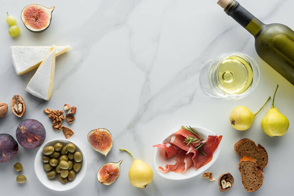 flat lay with wine, brie cheese, jamon and figs assorted on white marble tabletop