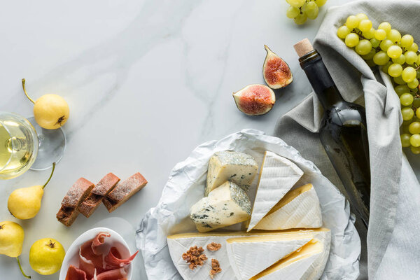 flat lay with wine, cheese, jamon and fruits arranged on white marble tabletop