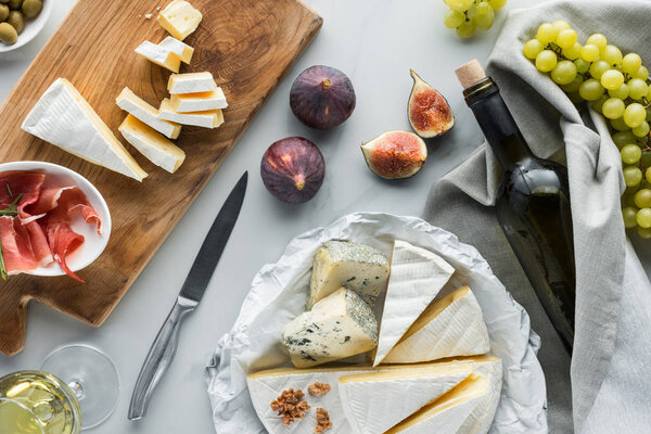 flat lay with wine, cheese, jamon, figs and grape arranged on white marble tabletop
