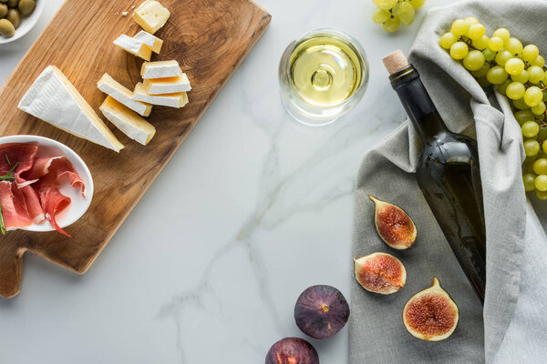 flat lay with wine, camembert cheese, jamon, figs and grape on white marble tabletop