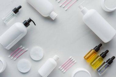 top view of bottles of cream, natural oils and cotton swabs on white tabletop, beauty concept