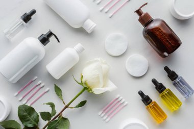 top view of bottles of cream, cosmetic pads and rose on white surface, beauty concept