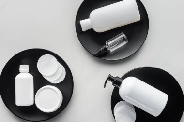 elevated view of bottles of cream and cosmetic pads on three black plates, beauty concept clipart