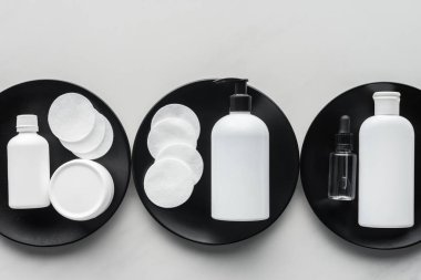 top view of bottles of cream and cosmetic pads on three black plates, beauty concept clipart