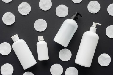 top view of scattered bottles of cream and cosmetic cotton pads isolated on black, beauty concept  clipart