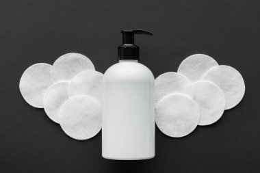 top view of bottle of cream and cosmetic pads isolated on black, beauty concept clipart