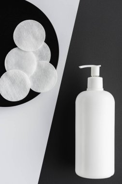 top view of bottle of cream and cotton pads on black and white surface, beauty concept clipart