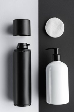 top view of bottles of cream and cosmetic pads on black and white surface, beauty concept clipart