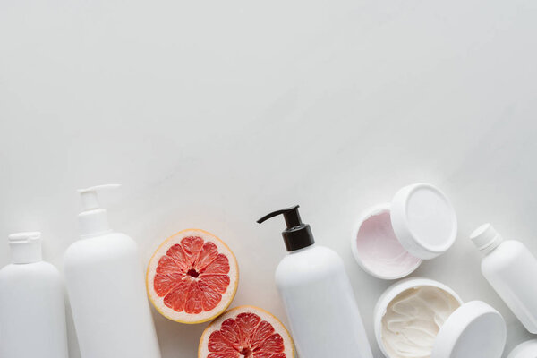 flat lay with containers of lotion and pieces of grapefruit on white surface, beauty concept