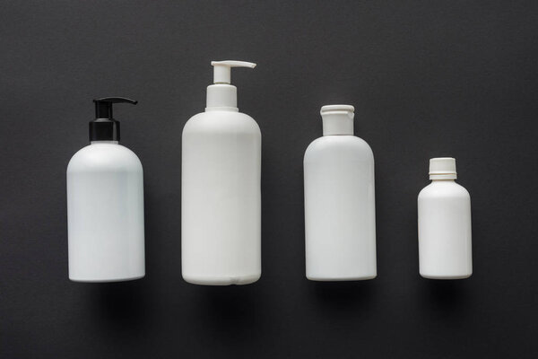 top view of four white bottles of cream isolated on black, beauty concept