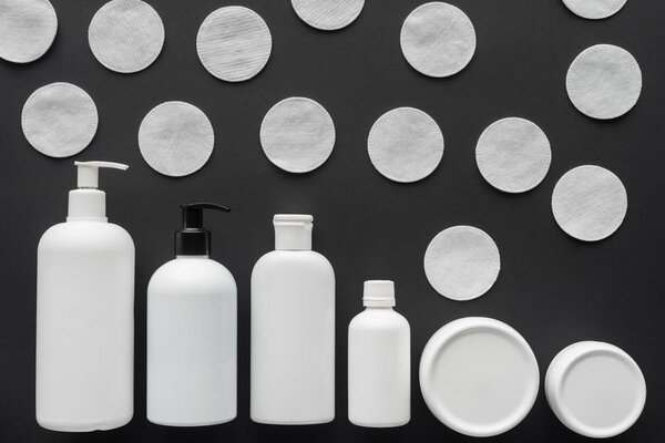 top view of bottles of cream and cosmetic cotton pads isolated on black, beauty concept 