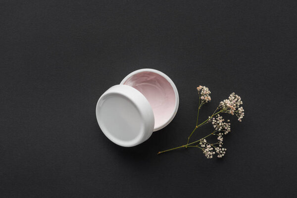 top view of bottle of cream and dried flowers isolated on black, beauty concept