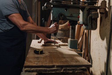 partial view of woodworker using electric drill on wood at workshop
