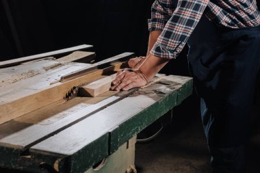 partial view of carpenter using saw at wooden workshop clipart