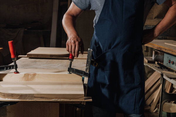 partial view of woodworker standing akimbo at wooden workshop