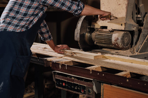 partial view of carpenter using saw at wooden workshop