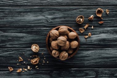 walnuts in wooden bowl with nutshells on dark wooden table clipart