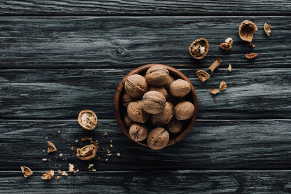 walnuts in wooden bowl with nutshells on dark wooden table