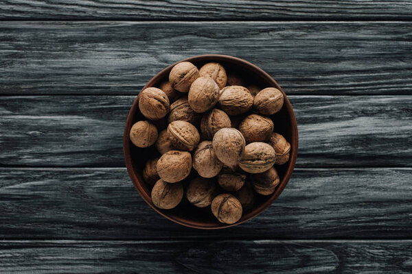 walnuts in wooden bowl on dark wooden background