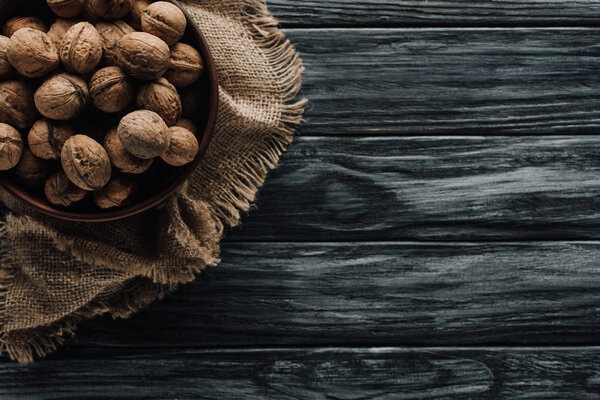 walnuts in wooden bowl on sackcloth on dark wooden surface