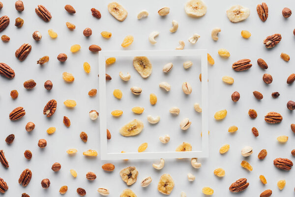 top view of white frame on dried fruits and nuts isolated on white background