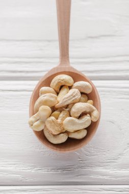 handful of cashew in wooden spoon on white wooden surface clipart