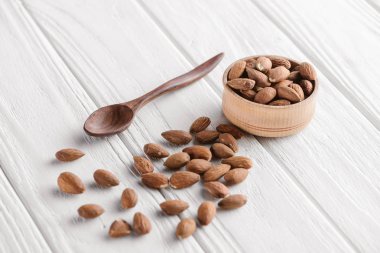 almonds with wooden bowl and spoon on white wooden table clipart
