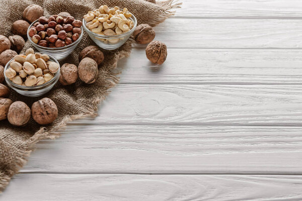 Ассорти орехов в стеклянных мисках на белом деревянном столе
