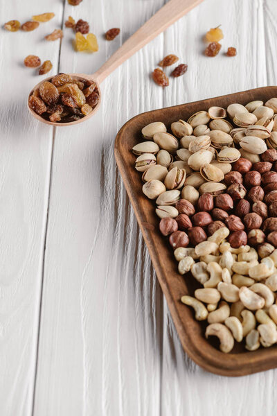 смесь орехов в тарелке и изюма в ложке на белом деревянном столе
