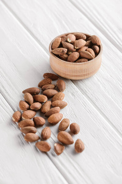 delicious almonds in wooden bowl on white wooden background