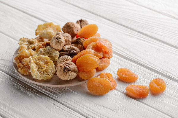 Mixed dried fruits on white plate on wooden table 