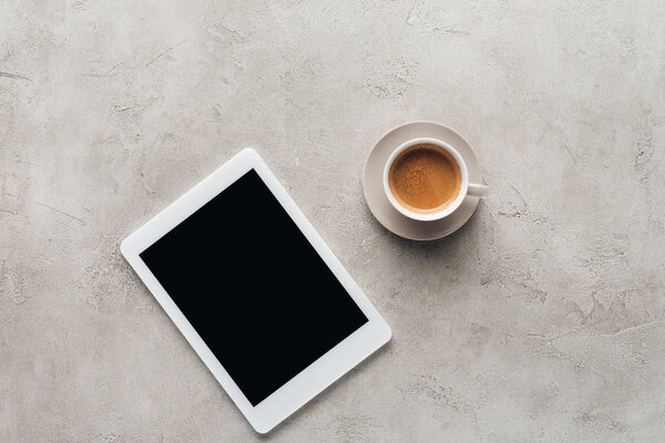 top view of cup of coffee and tablet with blank screen on concrete surface
