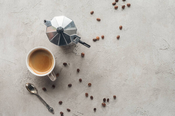вид сверху на чашку кофе и кофейник мока на бетонную поверхность с пролитыми кофейными зёрнами
