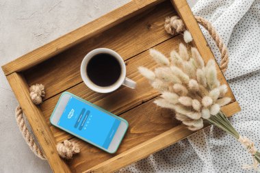 top view of cup of coffee and smartphone with skype app on screen on tray with lagurus ovatus bouquet on concrete surface clipart