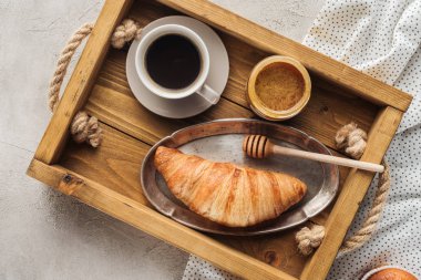 top view of cup of coffee with croissant and honey on tray on concrete surface clipart