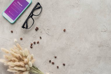 top view of smartphone with instagram app on screen with eyeglasses, spilled coffee beans and lagurus ovatus bouquet on concrete surface clipart