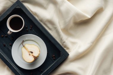 top view of cup of coffee with half of ripe pear on beige cloth, breakfast in bed concept clipart