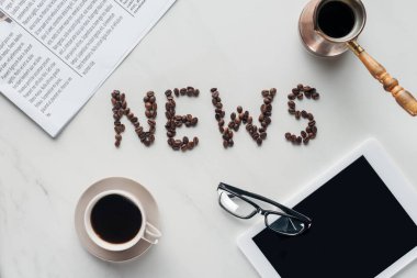 kahve kahve çekirdekleri ve beyaz mermer tablete gazeteyle yapılmış haber yazı ile üstten görünüm