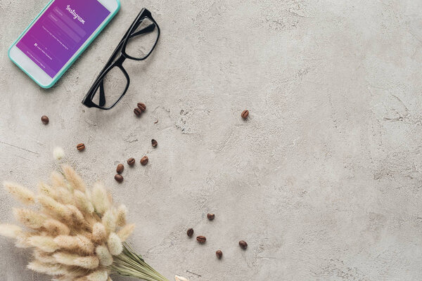 top view of smartphone with instagram app on screen with eyeglasses, spilled coffee beans and lagurus ovatus bouquet on concrete surface